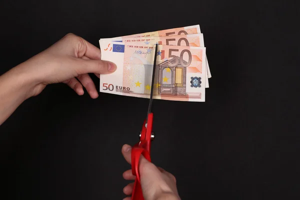 Hands with scissors cutting Euro banknotes, on black background — Stock Photo, Image