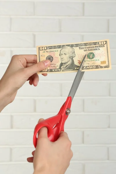 Manos con tijeras cortando dinero sobre fondo de pared de ladrillo blanco —  Fotos de Stock