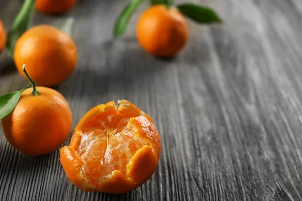 Gepelde vers mandarijnen met bladeren en rijpe mandarijnen op houten tafel, close-up — Stockfoto