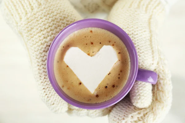 Mains féminines dans des mitaines chaudes tenant une tasse de cappuccino chaud avec guimauve cardiaque, gros plan — Photo