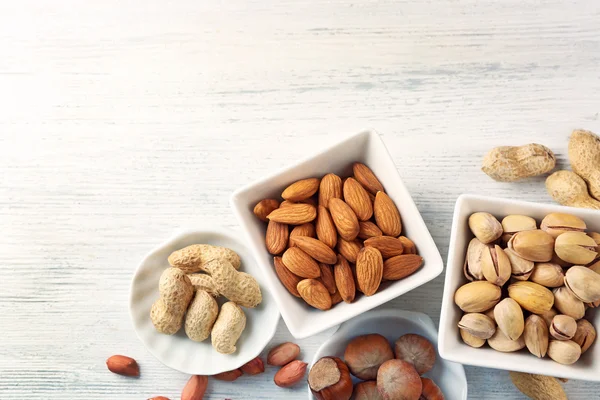 Pistagenötter, mandel, hasselnötter, jordnötter och nötkärnorna i den keramiska skålar, på vit trä bakgrund — Stockfoto