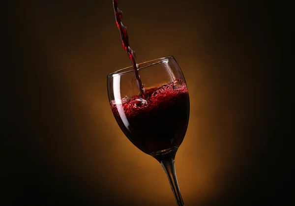 Вино выливается в стекло на коричневом фоне — стоковое фото