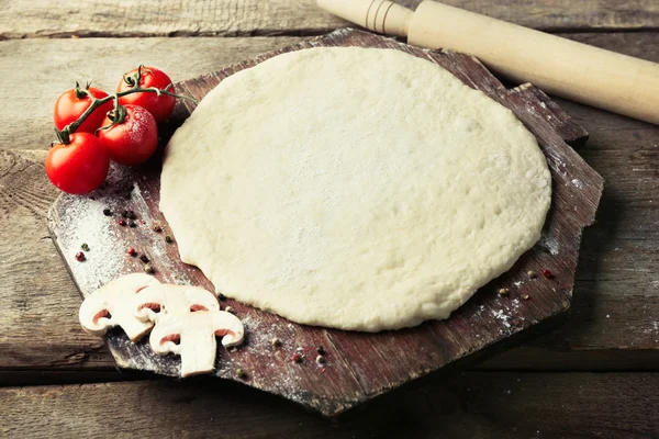 Massa de farinha fresca preparada para pizza com tomates e cogumelos fatiados em uma tábua de madeira, close-up — Fotografia de Stock