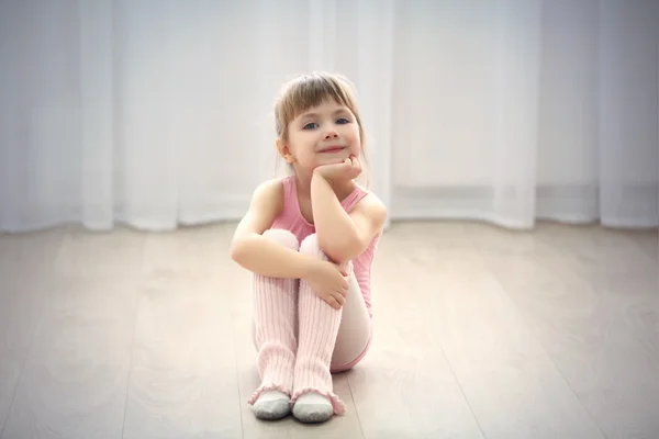 Pouco bonito menina em rosa leotard sentado no chão no estúdio de dança — Fotografia de Stock