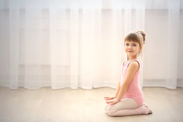 Little cute girl in pink leotard sitting on floor at dance studio