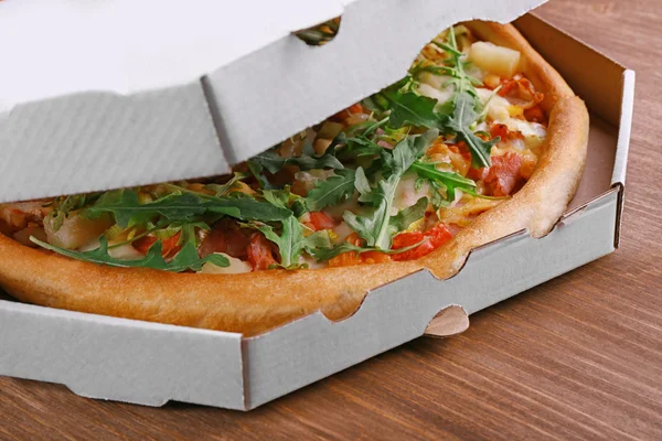Świeżej pizzy w karton na drewnianym stole zbliżenie — Zdjęcie stockowe