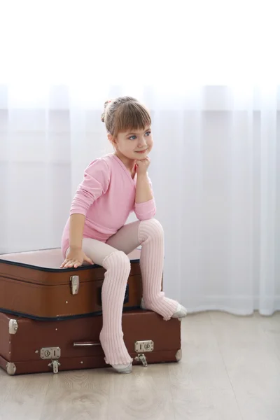 Niña linda en maillot rosa sentada en maletas en el estudio de baile — Foto de Stock