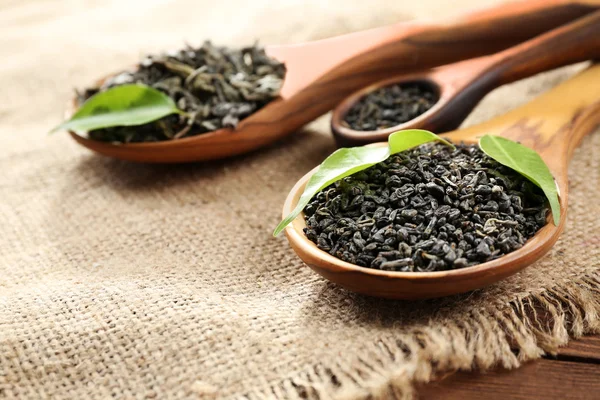 Suchej herbaty z zielonych liści w drewniane łyżki na płótnie tło — Zdjęcie stockowe