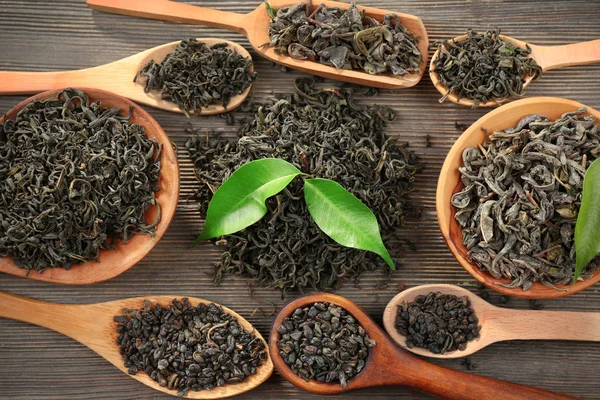 Té seco con hojas verdes en cucharas de madera sobre fondo de mesa —  Fotos de Stock