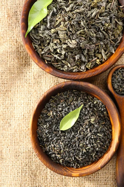 Dry tea with green leaves in wooden bowls on burlap background — Stock Photo, Image