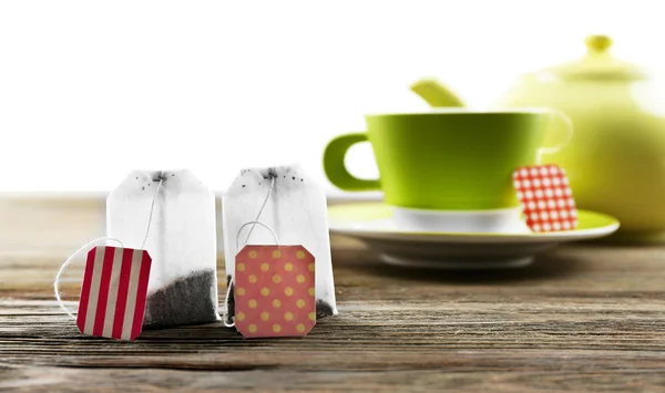 Cup of tea with tea bags and teapot on wooden background against grey background — Stock Photo, Image