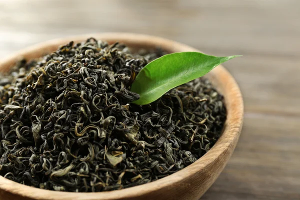Tè secco con foglie verdi in ciotola su sfondo tavolo di legno — Foto Stock