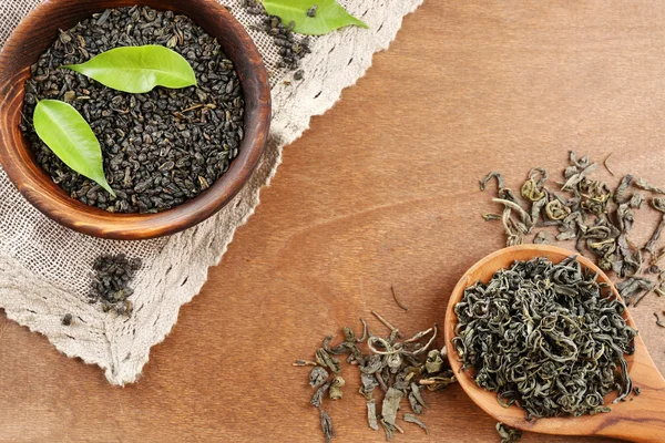 Trockener Tee mit grünen Blättern in Holzlöffel und Schüssel auf hölzernem Tischhintergrund — Stockfoto