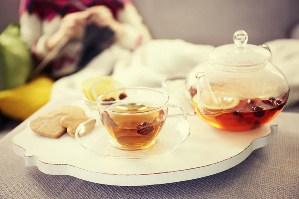 Xícara de chá e chaleira no tapete de madeira branco ao lado do sofá no fundo da mulher de tricô — Fotografia de Stock