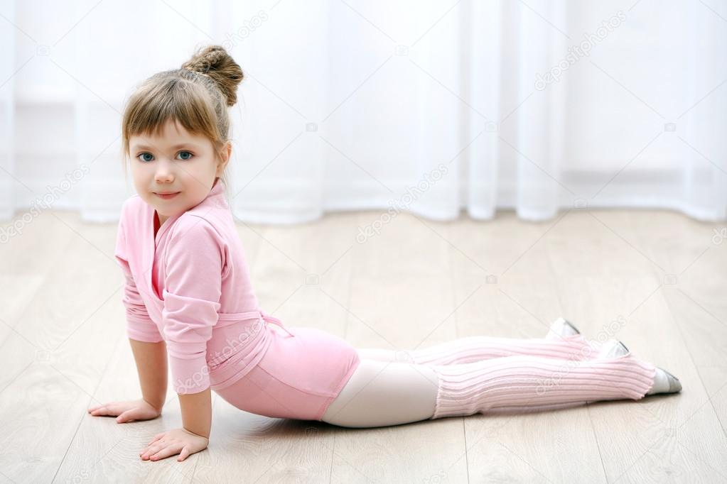 Little cute girl in pink leotard making new ballet movement at dance studio