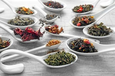 Gri ahşap arka plan üzerinde beyaz kaşık kuru çay çeşitli