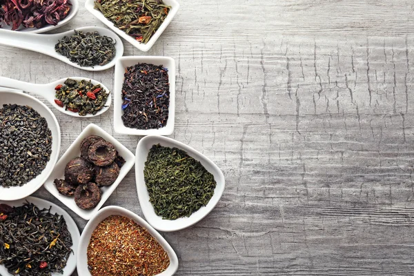 Mängd torr te i skålar och skedar på grå trä bakgrund, kopia utrymme — Stockfoto