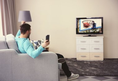 Genç adam evde televizyon izliyor.