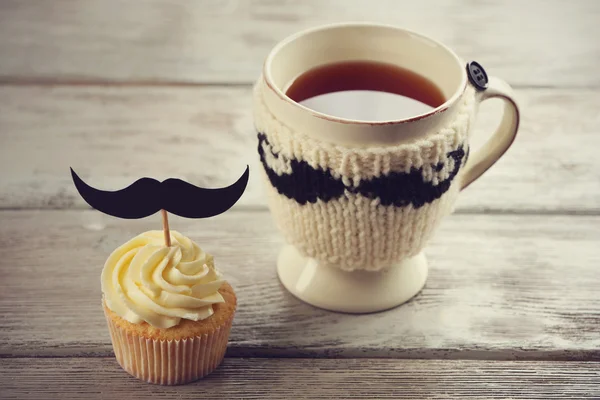 Läckra kreativa cupcake med mustasch och kopp te på träbord — Stockfoto