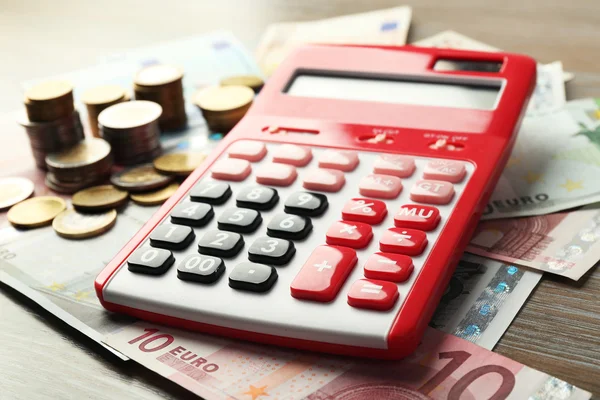 Money concept. Red calculator with banknotes and coins on wooden table — Stock Photo, Image