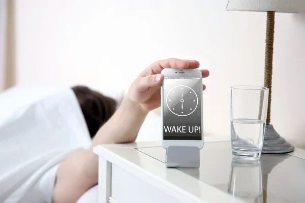 Jeune homme dormant dans le lit près de la table de chevet avec téléphone portable à la maison — Photo