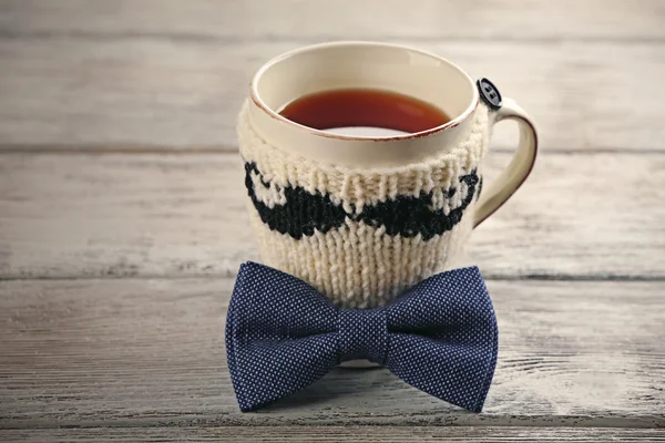 Bow tie and cup of tea with knitted mustache on wooden table — Stock Photo, Image