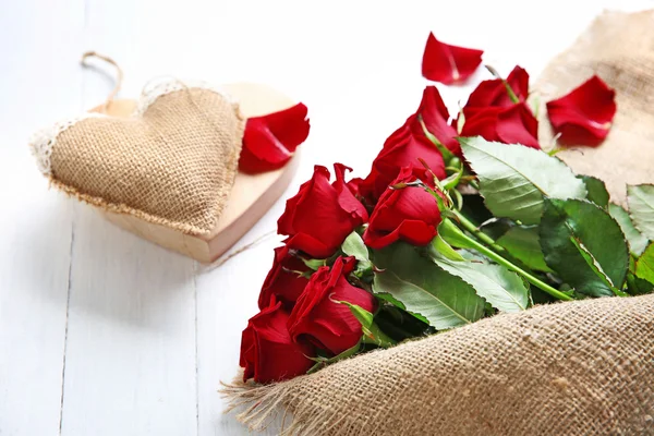Beautiful bouquet of red roses wrapped in sackcloth with heart on wooden background — Stock Photo, Image