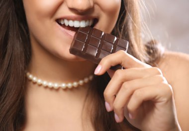 Loving chocolate woman bites bar to enjoy the taste, close up clipart