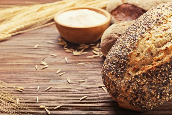 Pan recién horneado, un tazón de harina y espigas de trigo sobre el fondo de madera —  Fotos de Stock