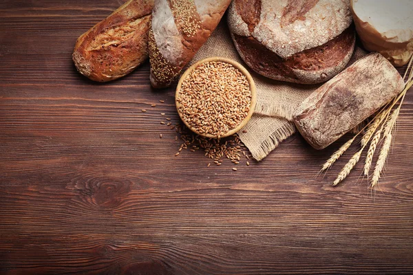 Pane appena sfornato e una ciotola di chicchi di grano sullo sfondo di legno — Foto Stock
