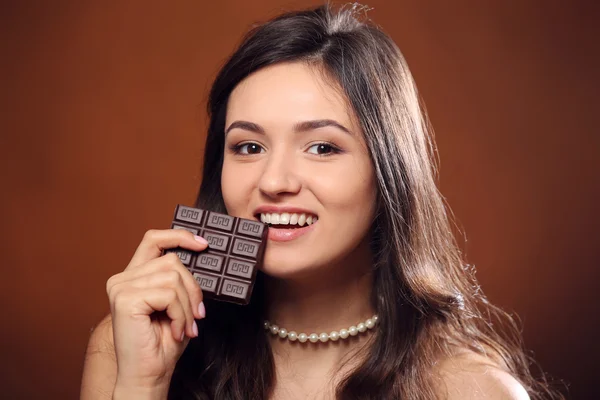 Portrait of attractive young woman with chocolate on brown background, close up — Stock Photo, Image