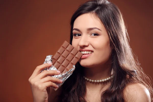 Portrait of attractive young woman with chocolate on brown background, close up — Stock Photo, Image