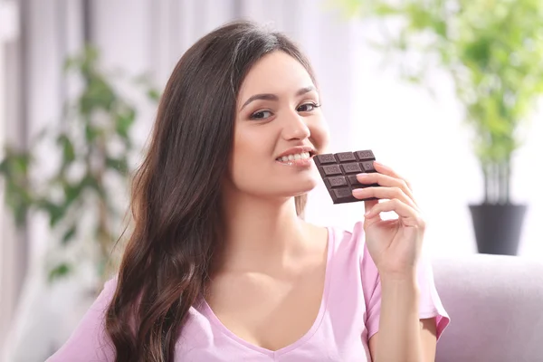 Retrato de bela jovem morena com chocolate no sofá na sala, close-up — Fotografia de Stock