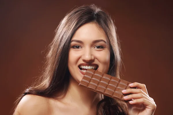Portrait of attractive young woman with chocolate on brown background, close up — Stock Photo, Image