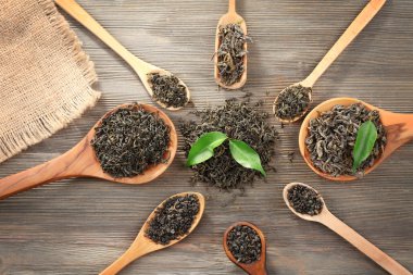 Tablo arka plan üzerinde tahta kaşıklar içinde yeşil yaprakları ile kuru çay