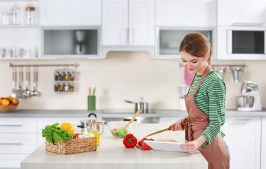 Genç bir kadın mutfakta yemek pişiriyor.