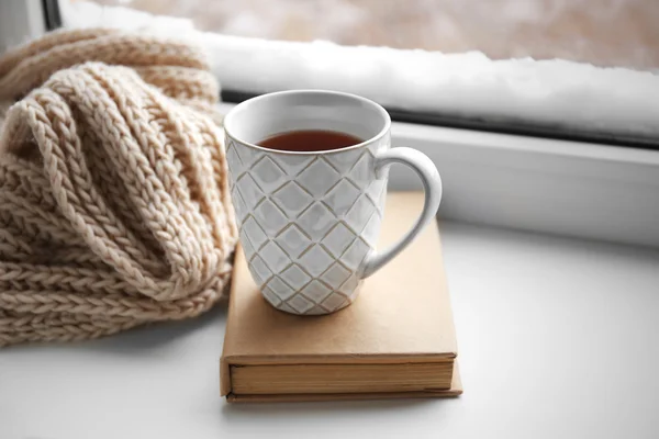Cup of tea, book and warm knitted scarf on windowsill, close up — Stock Photo, Image