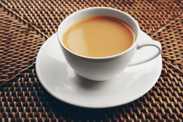 Porcelanowa filiżanka herbaty z mlekiem na tle wiklinowe — Zdjęcie stockowe
