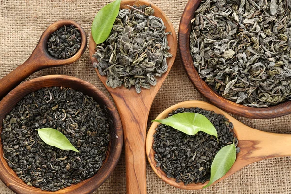 Té seco con hojas verdes en cucharas de madera sobre fondo de arpillera — Foto de Stock