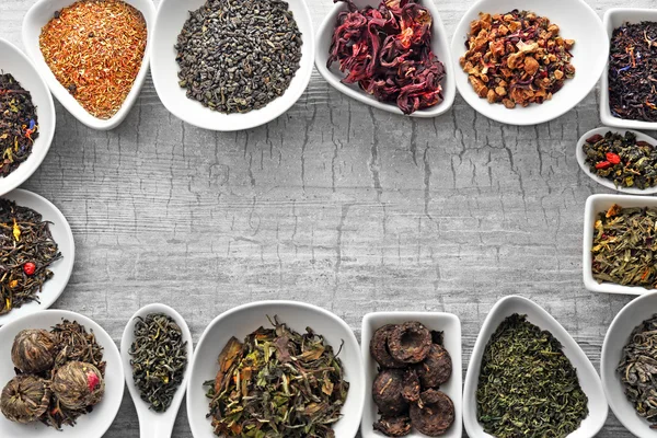 Variety of dry tea in bowls on grey wooden background, copy space — Stock Photo, Image