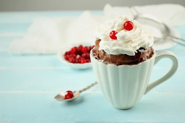 Mug cake with cream and cranberry on blue wooden background Royalty Free Stock Photos