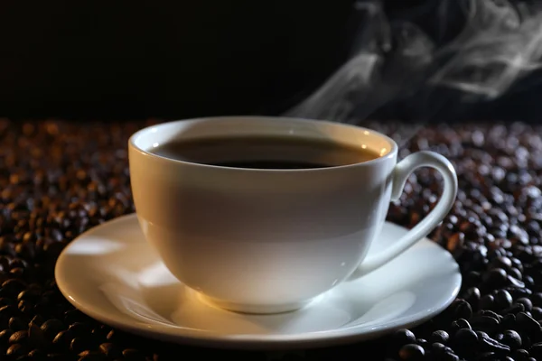 Taza de café caliente entre granos de café sobre fondo oscuro —  Fotos de Stock