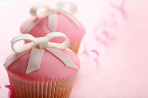 Cupcakes saborosos com arco na cor de fundo de madeira — Fotografia de Stock