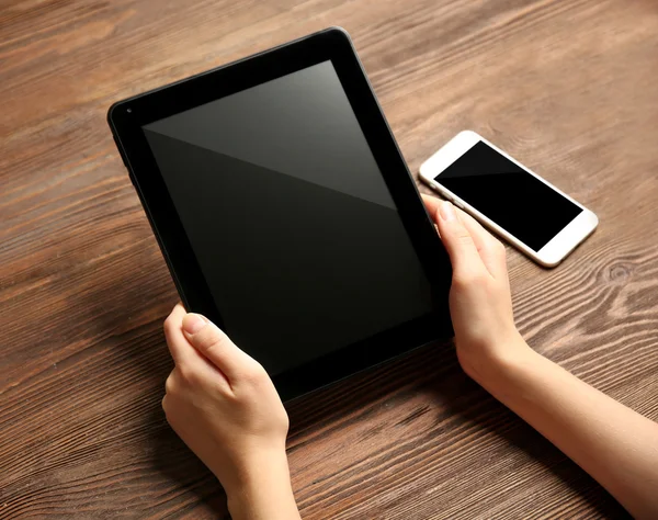 Мобильный телефон и женские руки с помощью планшета, на деревянном фоне — стоковое фото