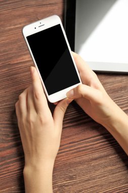 Bir tablet ve cep telefonuyla, ahşap arka plan üzerinde eller