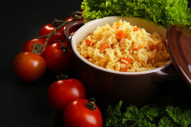 Bir havuç ve siyah arka plan üzerinde bir tencereye domates ile haşlanmış pirinç yakın çekim