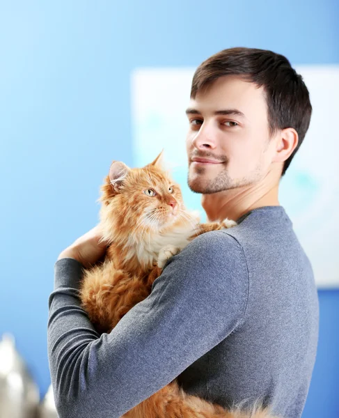 Kabarık kırmızı kedi tutan gülümseyen genç adam — Stok fotoğraf