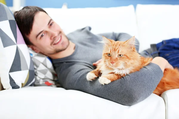 Joven con gato esponjoso tumbado en un sofá — Foto de Stock