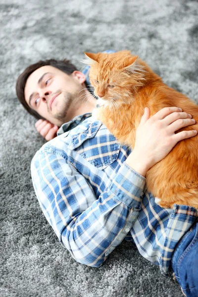 Young man with fluffy cat lying on a carpet — Stock Photo, Image