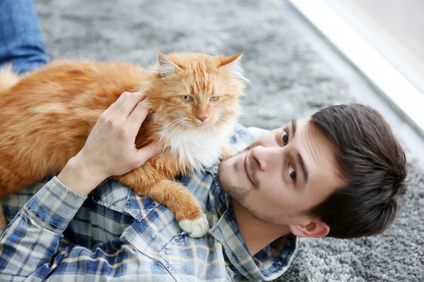 Jovem com gato fofo deitado em um tapete — Fotografia de Stock